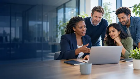 Four colleagues gathered around a laptop in an open-plan office, talking something through