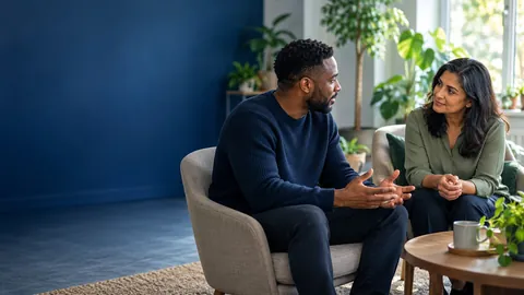 Two people talking quietly in armchairs in a bright room with plants