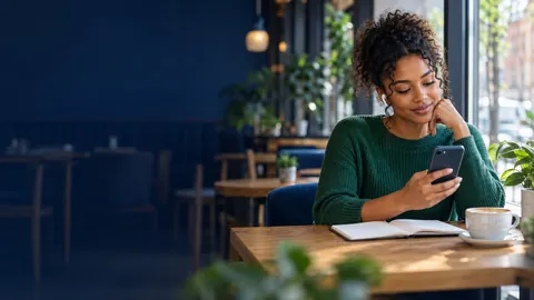 A woman in a cafe looking at her phone with a notebook and coffee on the table